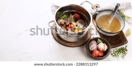 Beef broth of beef meat on bones slow cooked with vegetables: carrot, onion, garlic, and spices served in a pot on a white background with ingredients, top view. Panorama with copy space.