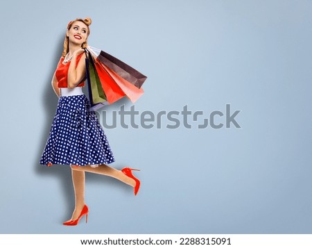 Full body of very happy, cheerful excited looking up woman in pinup dress holding, carrying many shopping bags, isolated against grey background. Sales discounts rebates or consumer bank credit ad.