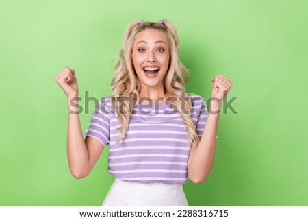 Photo of impressed cheerful girl curly hairdo dressed striped t-shirt raising fists fan support isolated on green color background