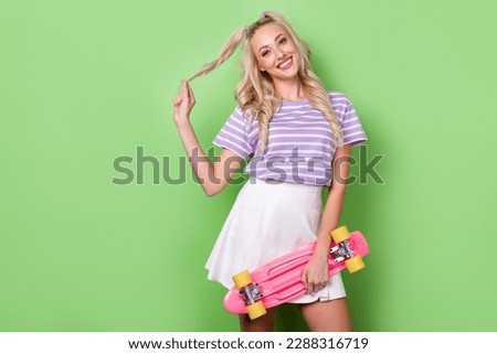 Portrait of pretty pleasant woman with wavy hairstyle dressed tabby t-shirt hold skateboard touching curl isolated on green color background