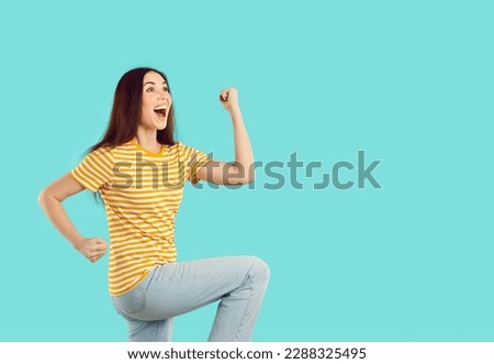 Happy crazy excited woman screams with joy clenching fists on light blue background. Young Caucasian woman in casual clothes having fun and rejoicing in her success standing near copy space. Royalty-Free Stock Photo #2288325495