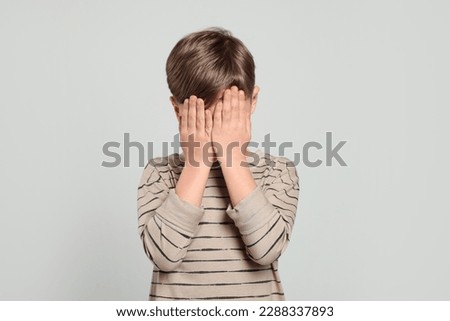 Boy covering face with hands on light grey background. Children's bullying Royalty-Free Stock Photo #2288337893