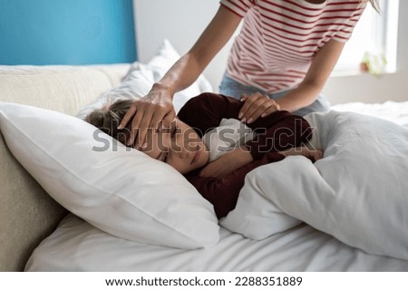 Sick little boy lying in bed, having chills and fever. Mother checking childs temperature touching forehead of unhealthy schoolboy son. Kid with respiratory illness symptoms. Childcare and influenza Royalty-Free Stock Photo #2288351889