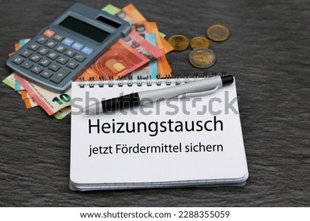 Money and notepad, application for grants for the energetic renovation of a property.German inscription means heating exchange now apply for grants. Royalty-Free Stock Photo #2288355059