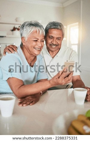 Phone, video call and elderly couple in a kitchen happy, smile and embrace in their home. Smartphone, love and old people pose for selfie, photo or profile picture while enjoying retirement together
