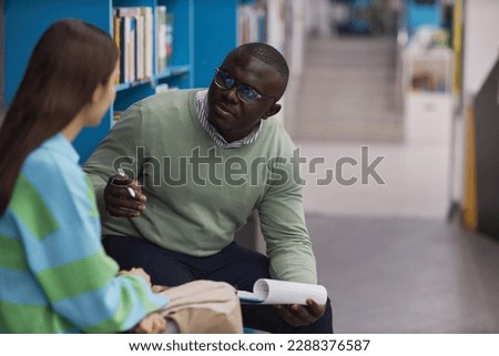Portrait of black young man as mental health therapist talking to teenage girl in college library, copy space