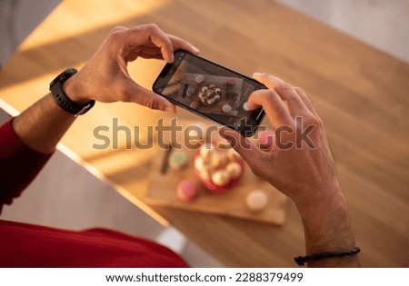 Unrecognizable man taking photo of pastry various cakes macaroons on wooden table, using cell phone, cropped of food blogger influencer shooting delicious desserts, copy space