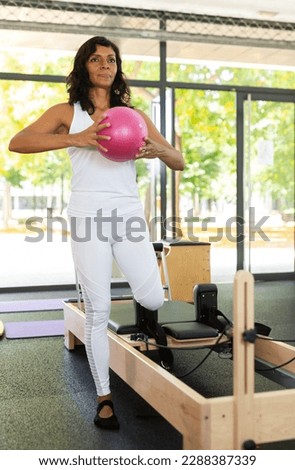 Portrait of positive hispanic woman practicing with pilates bender ball to strengthen muscles in fitness studio