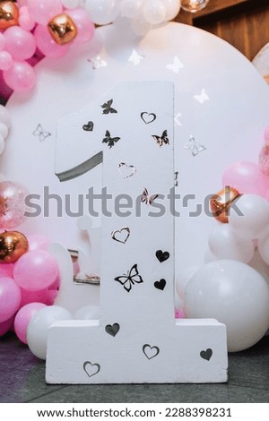 A large cardboard number one and multi-colored, pink, white balloons against the wall at a girl's children's birthday party. Photography, holiday, photo zone, copy space.