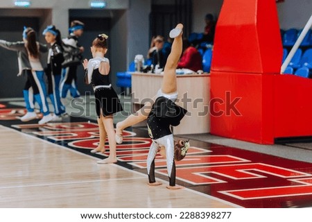A beautiful little girl, a child, a cheerleader sportswoman in a uniform, a colored dress dances, jumps, somersaults showing complex elements of gymnastics in the gym. Photography, sport concept. Royalty-Free Stock Photo #2288398277