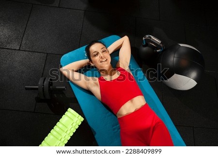 athletic woman in red sportswear lies on yoga matte in black gym and smiles, girl is relaxing on yoga matte, attractive woman in fitness club with fitness equipment Royalty-Free Stock Photo #2288409899