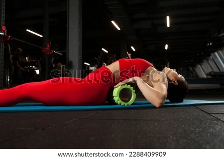 athletic woman in red sportswear doing back and spine exercise in black gym, girl training on yoga matte, attractive woman in fitness club doing back rolling Royalty-Free Stock Photo #2288409909
