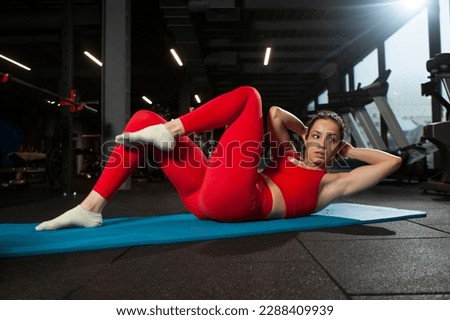 athletic woman in red sportswear is doing abs exercises in black gym, girl is doing sports on yoga matte, attractive woman in fitness club is doing exercise on the abdominal muscles Royalty-Free Stock Photo #2288409939