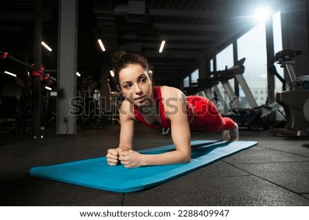 athletic woman in red sportswear doing plank in black gym, girl exercising on yoga matte, attractive woman in fitness club standing in plank Royalty-Free Stock Photo #2288409947