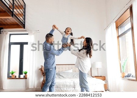 happy Asian family with little daughter stands at home in the bedroom and rejoices, dad and mom raise the hands of cheerful child in their house Royalty-Free Stock Photo #2288412153