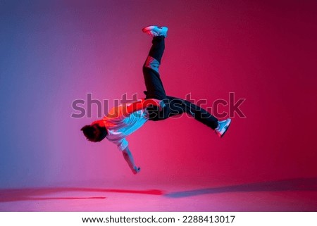 guy acrobat doing back fat in new lighting, male dancer jumps and falls in the air on red blue background, hiphop performer does trick and levitates in the air