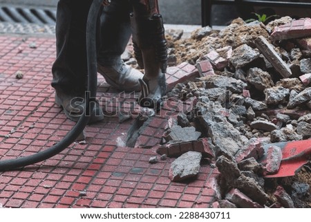 Process of sidewalk road repairing with jackhammer, builder worker with pneumatic hammer and drill equipment breaking asphalt pavement and concrete at construction site, during new walkway works