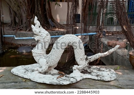 Closeup of White Naga stone statue Located beside a pond under a banyan tree background within Thai Buddhist Temple in Bangkok, Thailand.