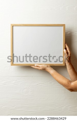 Vertical of hands holding empty wooden frame with copy space against white wall. Mock up frame template, interior design and decoration.