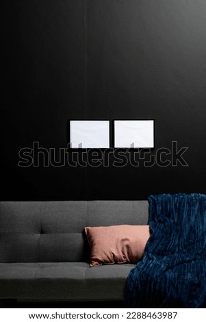 Vertical of empty white canvases with copy space on black wall in room with couch. Mock up frame template, interior design and decoration.