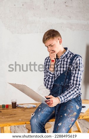 Thoughtful painter or artist In a denim overalls and checkered shirt looking and thinking about his art or painting.