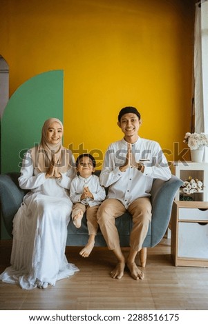Portrait of Asian Muslim parents and son smile with greeting gesture sitting on sofa
