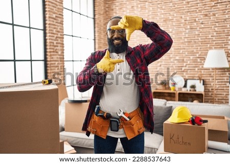 African american man working at home renovation smiling making frame with hands and fingers with happy face. creativity and photography concept. 