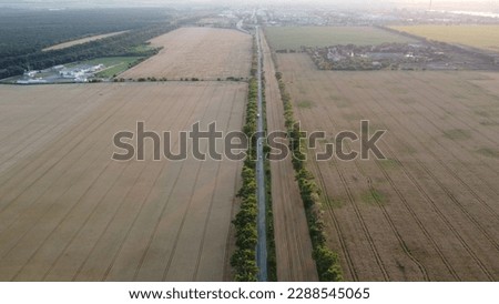 Beautiful panoramic landscape agricultural fields of ripe wheat,road with moving cars, industrial plants, forest, city on summer evening. Agricultural agrarian scenery. Aerial drone view. Top view.
