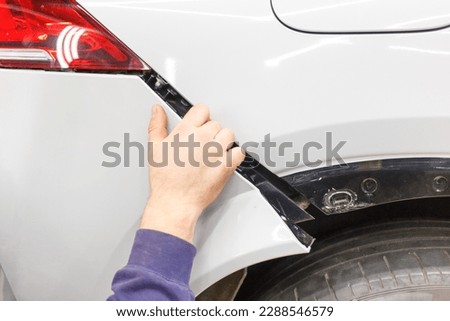 The master mechanic installs the bumper on the car. An auto mechanic repairs the car body by replacing the bumper. The hand of the mechanic installing the bumper on the car after repair. Royalty-Free Stock Photo #2288546579