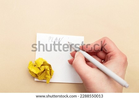 Female woman hand writing a plan or to do list on piece of paper for notes with a crumpled yelllow paper like a bulb as a concept creative idea and innovation on beige background