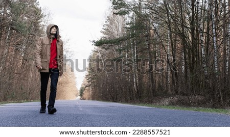 Tinted portrait image of a young guy in a hooded jacket on a forest road outside the city