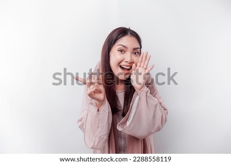 Young beautiful Asian Muslim woman wearing a headscarf shouting and screaming loud with a hand on her mouth. communication concept.