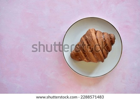 French Croissant on a white plate. Everything on a pinkish backdrop. Perfect for breakfast or afternoon tea. 