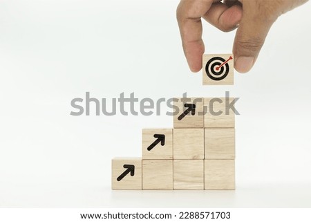 Hand stacking virtual target and arrow icons on wooden cube. Business achievement goal and objective target concept.
