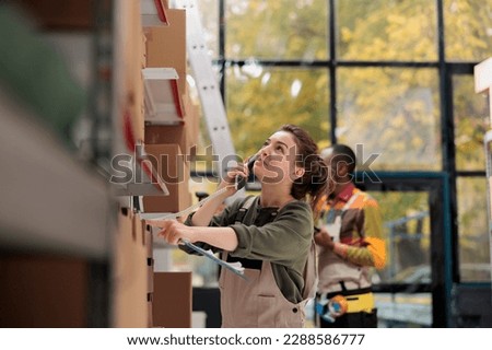 Storage room worker talking at landline phone with remote supervisor, working at packing clients order while doing warehouse inventory. Woman doing products quality control in delivery department Royalty-Free Stock Photo #2288586777