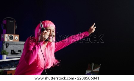 Musician having fun during performance talking with fans, mixing and mastering electronic sound using professional mixer console. Dj artist with pink hair performing music in club at nightime