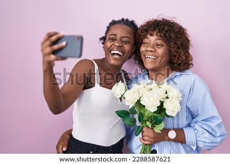 Two african women taking a selfie photo with flowers smiling and laughing hard out loud because funny crazy joke. 
