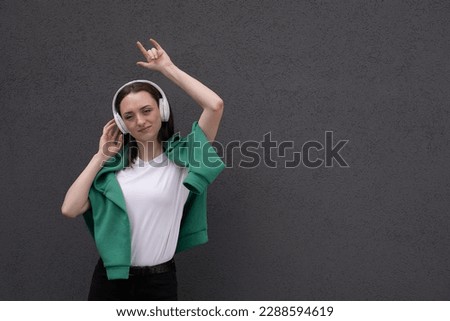 A young teenager girl listens to music with headphones, dressed in a gray jacket and black jeans, dances to the music and sings songs loudly
