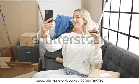 Young blonde woman taking selfie picture by smartphone and drinking wine at new home