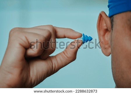 closeup of a swimmer man, wearing a blue swimming cap, about to put an earplug, in a swimming pool Royalty-Free Stock Photo #2288632873
