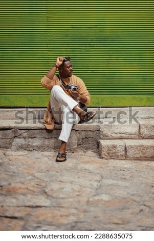 A beautiful African tourist is hanging out in the downtown area. He is about to take some pictures with his camera