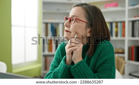 Mature hispanic woman with grey hair thinking at library