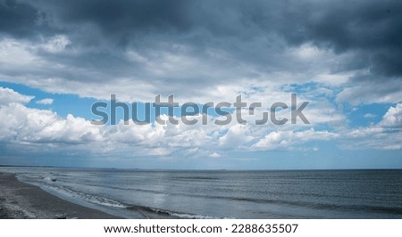 Sea shore line with dark clouds, blue sky and dark waters. Panoramic empty beach landscape.