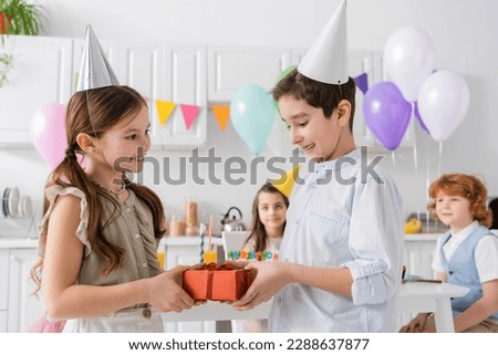 happy preteen boy in braces giving present to cheerful birthday girl near friends on blurred background