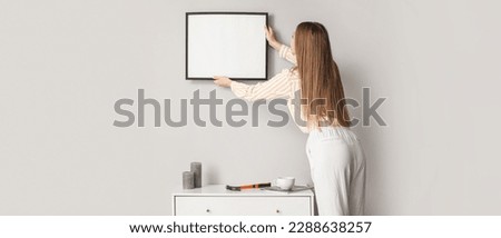 Young woman hanging blank picture on wall in room