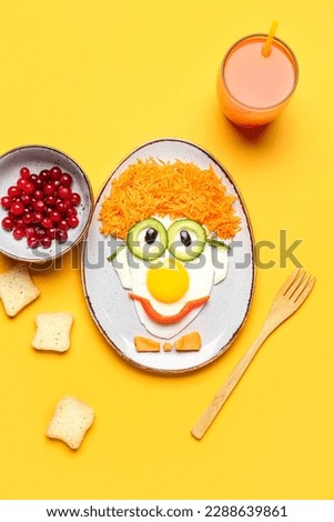 Plate with funny breakfast in shape of clown, berries and glass of juice on orange background