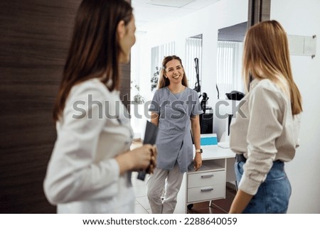 Joyful female beautician meets her new client. Three women communicate and smile at each other. Welcoming young girl in casual clothes in beauty salon. Light modern interior in clinic. Copy space. Royalty-Free Stock Photo #2288640059