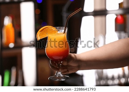 Woman holding glass of tasty Tequila Sunrise in bar