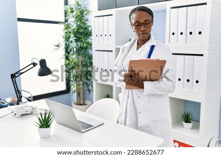 African american woman doctor smiling confident writing medical report at clinic