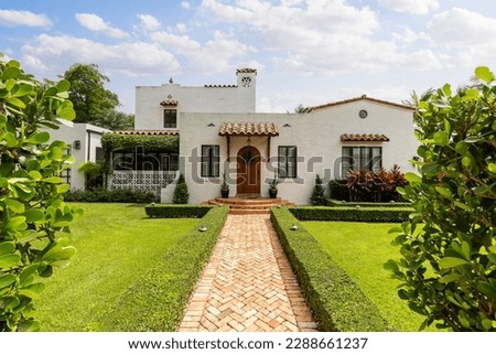 Facade of an elegant colonial-style house, white walls with details in reddish tiles and paths, short grass, privet, palms, blue sky.
Located in Coral Gables, Miami, FL, USA Royalty-Free Stock Photo #2288661237